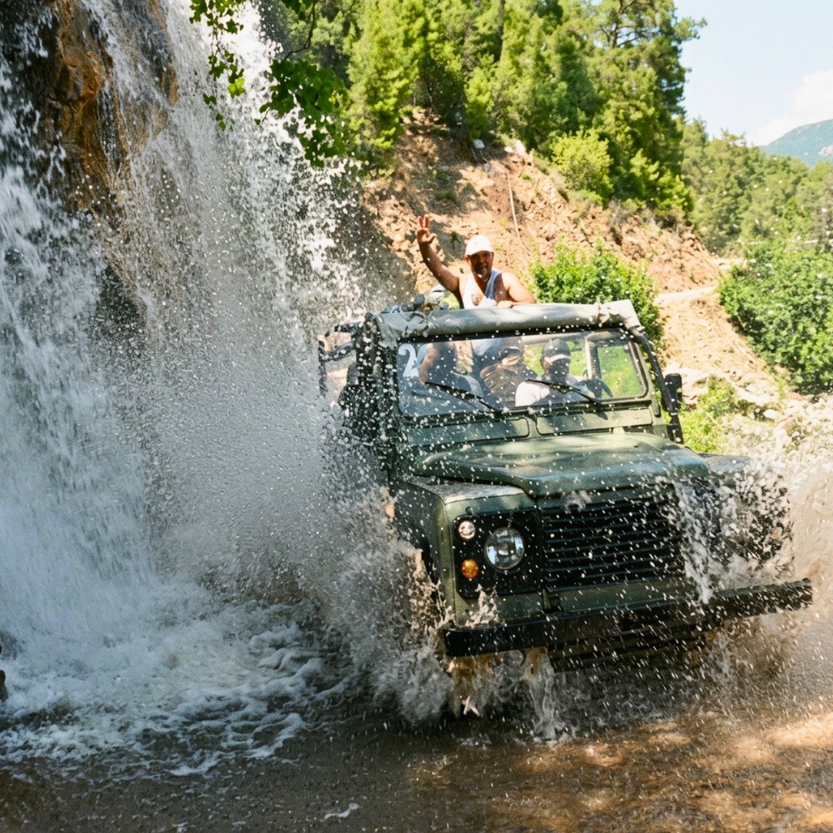 Jeep splashing through water under a waterfall