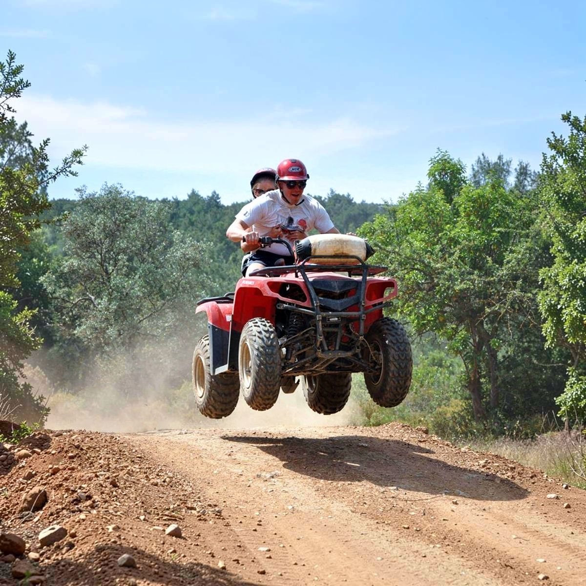 Quad riders on dirt track with mountain backdrop