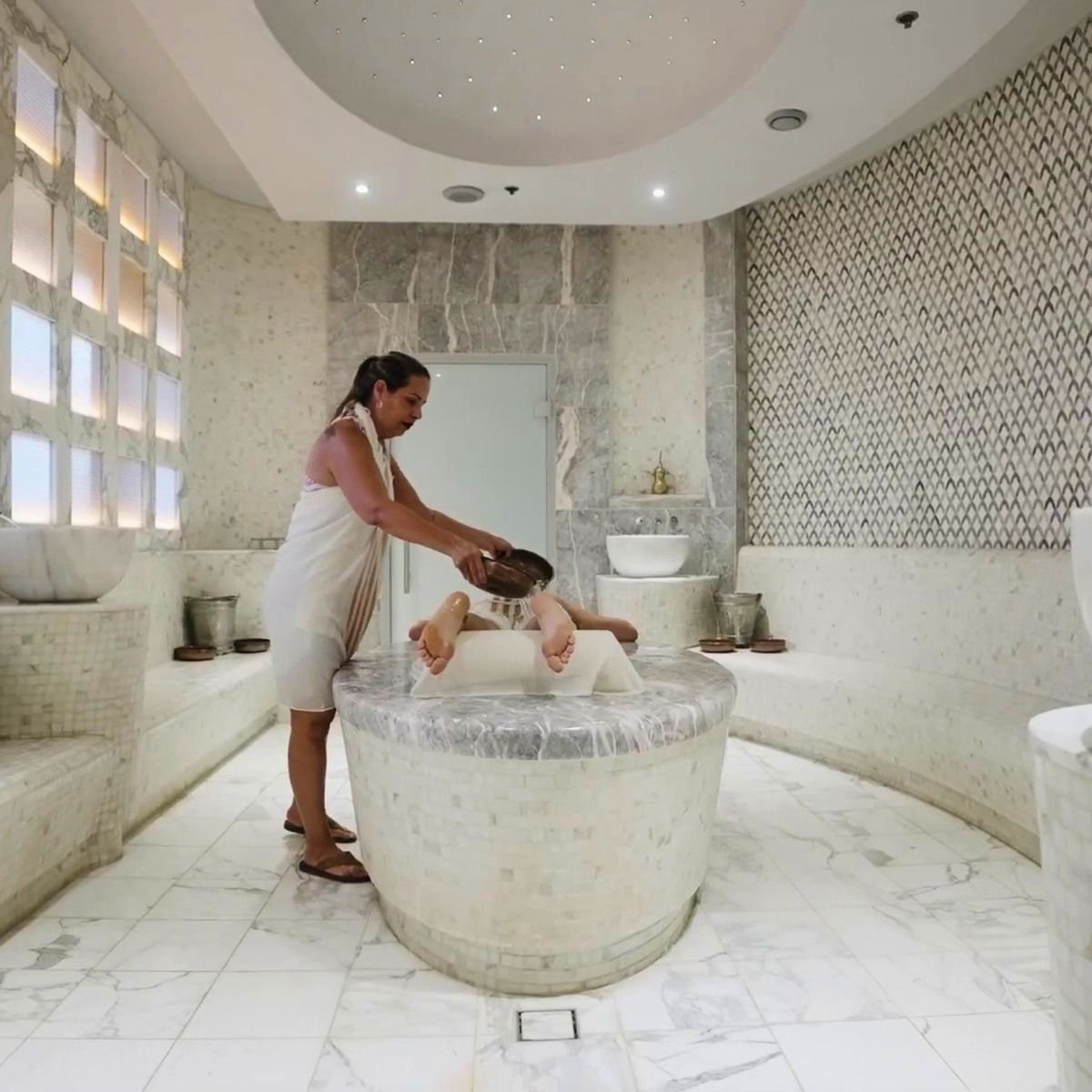 Guest receiving traditional foot rinse on marble göbektaşı in a luxury hamam
