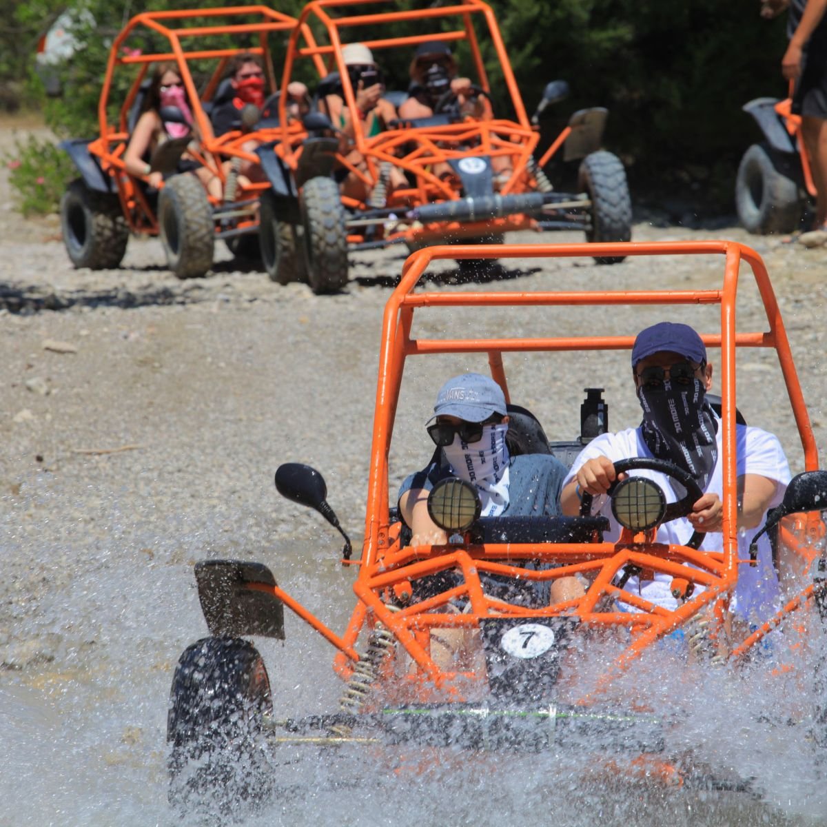 Orange buggies splashing through water on dirt track